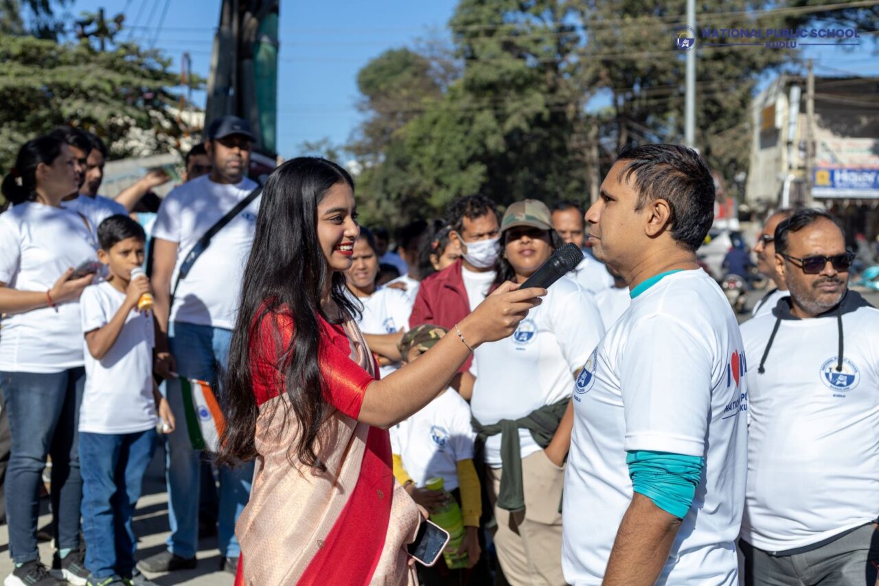 The event host is engaging the crowd while they were marching towards the NPS kudlu campus on the Walkathon event which was organised for Republic Day by National Public School Kudlu.